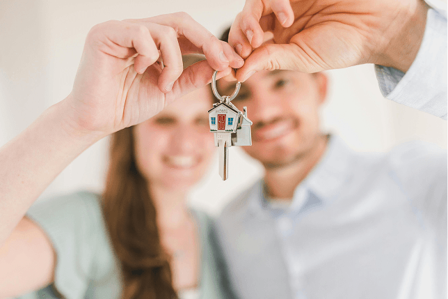 A couple hold up a set of house keys with a house-shaped keychain